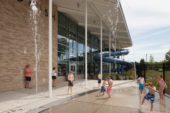 A spray feature draws children outside. The strong horizontal roof helps provide shade and mitigates glare for comfort and energy efficiency.